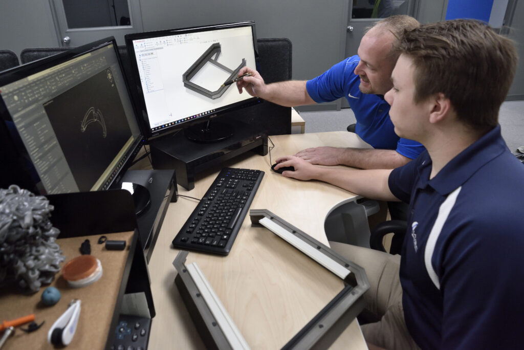 Two employees are sitting at a desk and examining mock up drawings of a product.